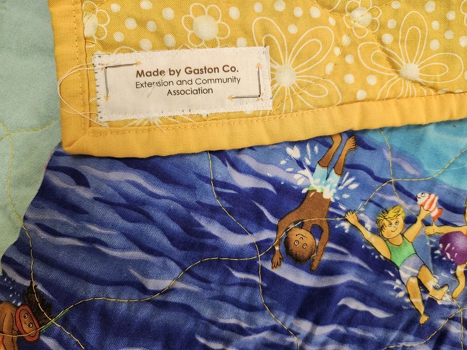 The back corner of a baby quilt is flipped over to show the ECA Quiltmakers label sewn in the corner.