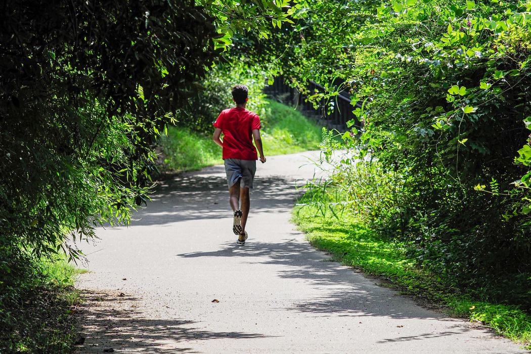 Someone jogging down an asphalt path wearing a red tshirt and shorts