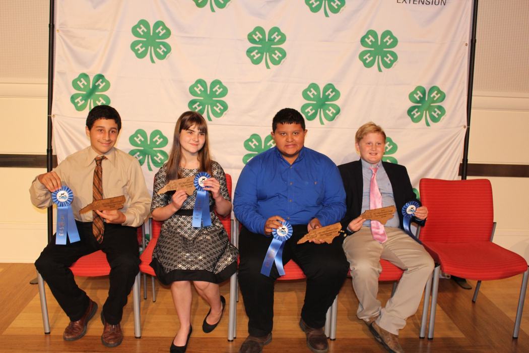 Several students posed in front of 4-H clover background holding ribbons and plaques for 2022 NC State 4-H Livestock awards.