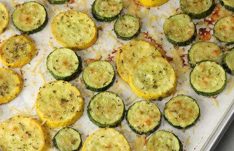 Roasted zucchini and yellow squash slices seasoned with herbs and lightly sprinkled with melted cheese, arranged on a parchment-lined baking sheet until golden and tender.