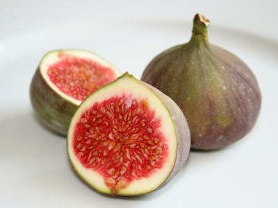 Whole fig and two halves showing red flesh and seeds on a white plate