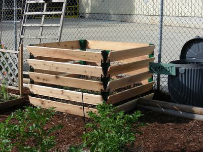 Wooden slatted compost bin with green sign reading COMPOST beside a trash can