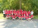 Large group of youths and adults wearing red event T-shirts posing outdoors under tree