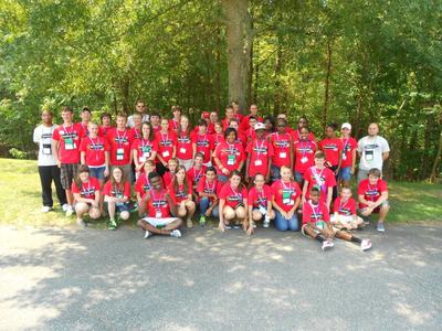 Large group of youths and adults wearing red event T-shirts posing outdoors under tree