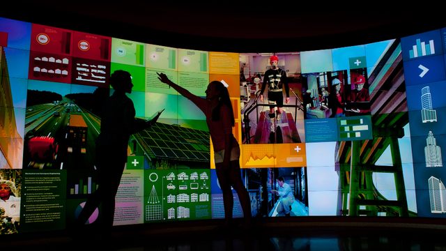 Two silhouettes pointing at a large multicolored infographic video wall