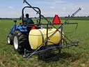 Blue tractor with rear-mounted yellow crop sprayer tank and extended booms in a field