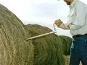 Man inserting a hay hook into a large round straw bale outdoors