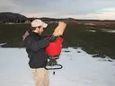 Man pouring bagged seed into red broadcast spreader on snowy field
