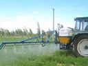 Tractor with rear-mounted boom sprayer spraying a green field