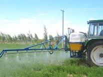 Tractor with rear-mounted boom sprayer spraying a green field