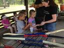 Instructor showing archery equipment to children; multiple bows laid on table