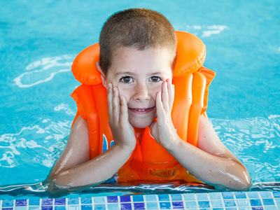 Child wearing orange swim float, hands on cheeks while leaning at pool edge