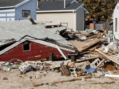 Collapsed red beachfront house surrounded by rubble, cinderblocks, and debris
