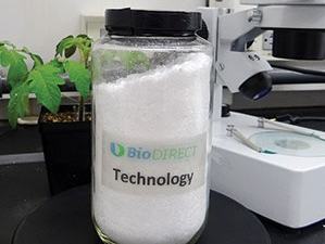 Jar labeled 'BioDIRECT Technology' with white powder on lab bench beside microscope