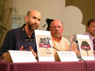 Five-person panel seated at a table with microphones; one man speaking and gesturing.