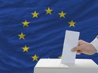 Hand inserting ballot into ballot box with European Union flag in background