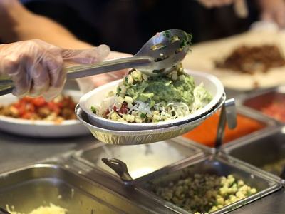 Gloved hand scooping guacamole onto rice bowl at a burrito serving counter