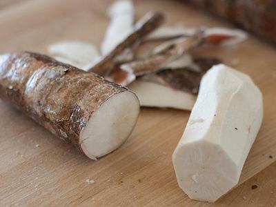 Cassava root pieces, one peeled and one unpeeled, on a wooden cutting board