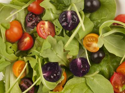 Arugula leaves with halved red, orange, and purple cherry tomatoes