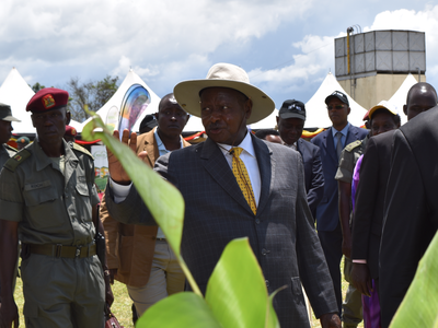 Man in suit and wide-brim hat gesturing while walking among officials outdoors
