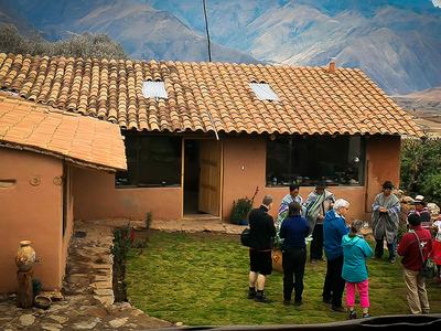 People gathered in courtyard of adobe house with tiled roof and mountains behind