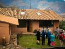 People gathered in courtyard of adobe house with tiled roof and mountains behind