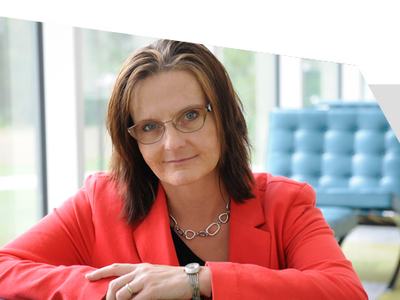 Woman in glasses and red blazer leaning on chair armrest in modern office lounge