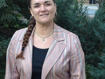 Woman with braided hair wearing a striped blazer standing outdoors near bushes