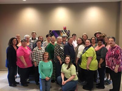 Large group of adults standing and kneeling in a hotel meeting room for a group photo