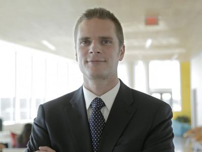 Man in suit and tie standing with arms crossed in a bright office corridor