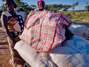 Two women beside a cart loaded with white sacks and a large red-striped bag