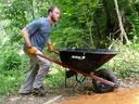Person wearing "GET OUT" shirt and gloves pushes a Jackson wheelbarrow on a wooded path