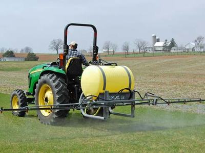 Tractor with rear-mounted yellow tank spraying a grassy field