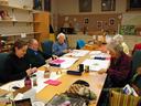 People seated around a long table working on crafts in a community room