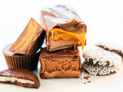 Assorted chocolate candies stacked; caramel oozing from a bitten chocolate bar