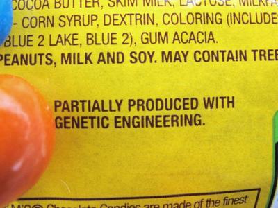 Yellow candy package label: "PARTIALLY PRODUCED WITH GENETIC ENGINEERING" with orange and blue candies