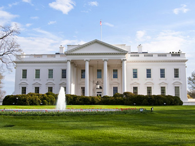 White House north facade with fountain, manicured lawn, and flag overhead