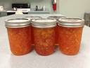 Six sealed mason jars filled with orange jam on a kitchen countertop