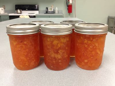 Six sealed mason jars filled with orange jam on a kitchen countertop