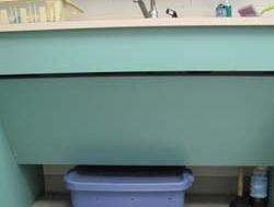 Green sink cabinet with a blue plastic storage bin positioned beneath the sink