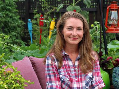 Woman sitting on outdoor cushion in a garden, wearing a red plaid shirt