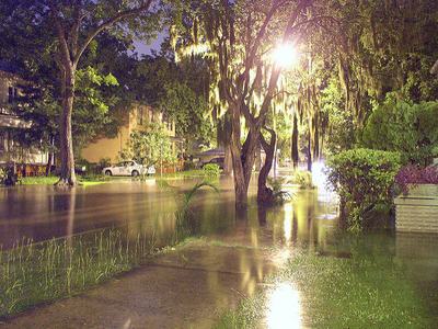 Residential street flooded at night, water covering sidewalks and parked cars
