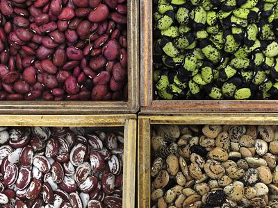 Four wooden bins holding four varieties of dried beans: red, green-black, maroon-white, tan-speckled