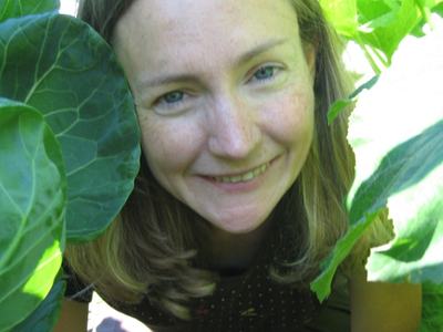Person crouching among large green leaves in a garden, facing the camera.