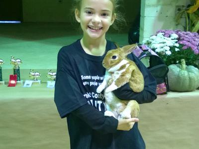 Girl holding brown-and-white rabbit in a hall with trophies and flowers