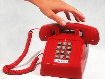 Hand lifting receiver of red desk phone labeled "EMERGENCY".
