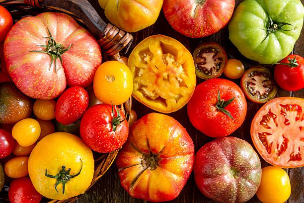 Assorted colorful heirloom tomatoes, whole and sliced, arranged on a wooden surface