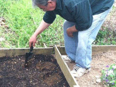 Person using a hand trowel to dig soil in a wooden raised garden bed