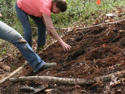 Person bending to work soil in a garden bed with an orange flag nearby