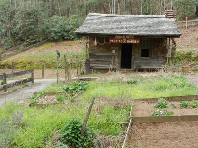 Log cabin with sign "Indian Herb and Vegetable Garden" and foreground raised garden beds